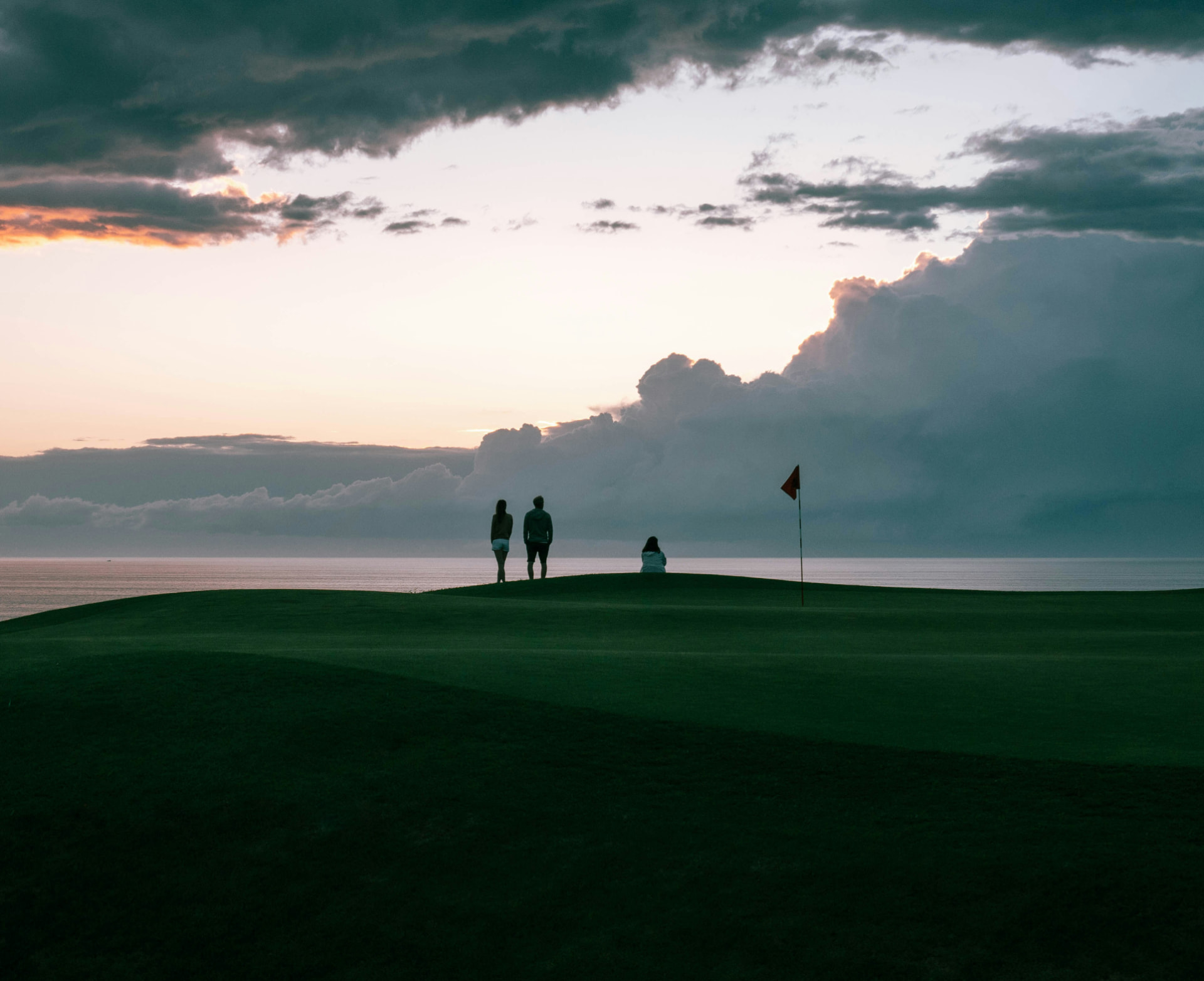 Players on a green above the sea at dusk