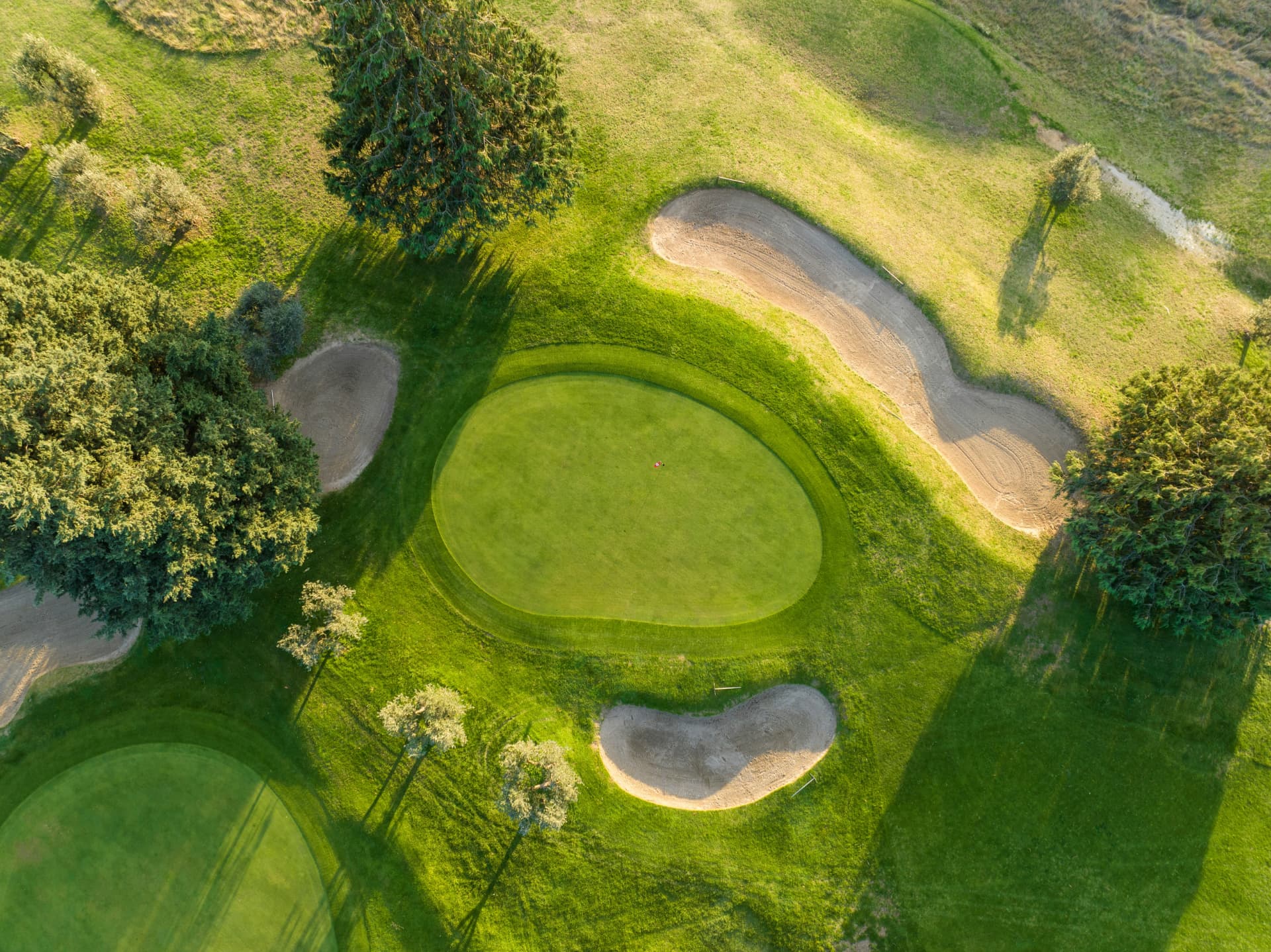Aerial view of a golf green ringed by sand bunkers in late afternoon light